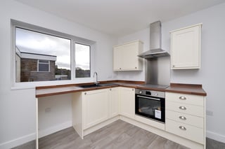 Modern kitchen with cream cabinets, dark wood countertops, stainless steel appliances, and large windows overlooking a garden