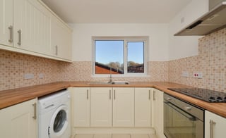 Modern cream-colored kitchen with wooden countertops, window, washing machine, and integrated appliances