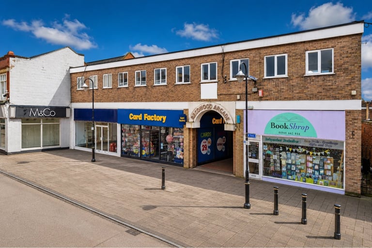 Row of retail storefronts with brick and white facade including Card Factory and Book Store, on a clear sunny day with blue sky