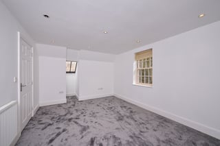 Empty room with white walls, gray carpeting, door on left, two windows, and recessed ceiling lights