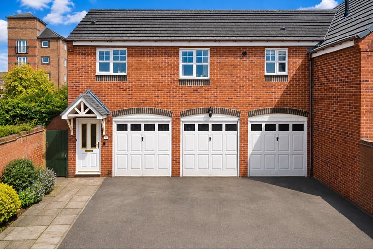 Modern red brick house with three white garage doors, front entrance, and manicured gardens on a paved driveway