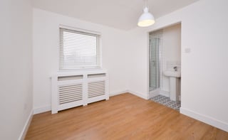 Empty modern living room with wooden floor, white walls, window with blinds, radiator, pendant light, and doorway