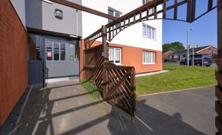 Residential building exterior with wooden pergola, brick walls, white door, and manicured lawn in bright daylight