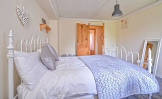 Bright bedroom with white metal bed frame, blue and white bedding, decorative pillows, and wooden door visible in background