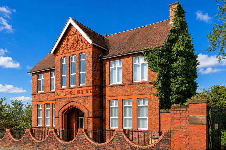 Red brick historic building with ivy-covered tower, gothic windows, and decorative rope fencing under blue sky