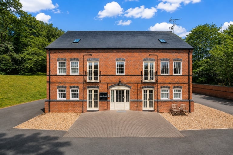 Modern red brick two-story residential house with white-framed windows and black slate roof, surrounded by green lawn and driveway