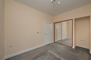 Empty bedroom with cream walls, gray carpet, white doors, and sliding wardrobe mirror on the right side