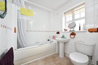 Clean bathroom with white tile walls, pedestal sink, toilet, bathtub with glass shower enclosure, and window with natural light