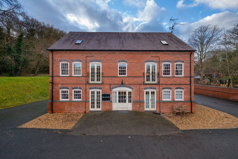 Large red brick two-story residential house with white trim and dormer windows, situated on manicured grounds with gravel driveway