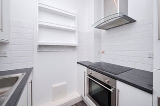 Modern kitchen with white subway tile walls, built-in oven, black countertops, open shelving, and stainless steel range hood