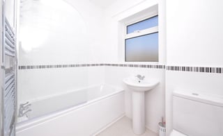 Modern white bathroom with bathtub, pedestal sink, toilet, and decorative tile border strip