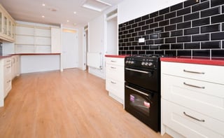 Modern kitchen with white cabinets, black subway tile backsplash, black double oven, red countertop trim, and wooden flooring