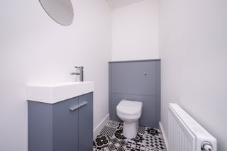Modern bathroom with gray cabinetry, white sink, toilet, black and white floor tiles, and white radiator