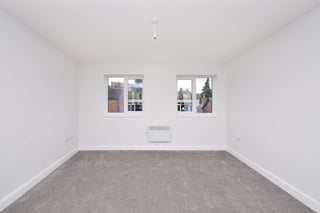 Empty room with white walls, gray carpet, two framed pictures on wall, light fixture on ceiling, and white outlet