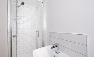 Modern minimalist bathroom with white subway tile shower enclosure, glass door, and white porcelain sink with chrome fixtures