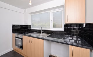 Modern kitchen with light wood cabinets, black tile backsplash, granite countertop, stainless steel oven, and window above sink