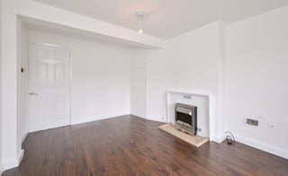 Empty living room with dark wood flooring, white walls, fireplace, and white door