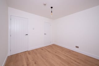 Empty room with white walls, wooden laminate floor, two white doors, and ceiling light fixture