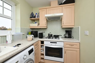 Compact kitchen with light wood cabinets, white appliances, mosaic tile backsplash, and granite countertops