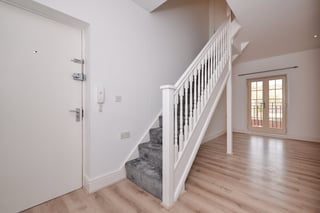 Modern staircase with white banister in a bright entryway with wooden floors and white door