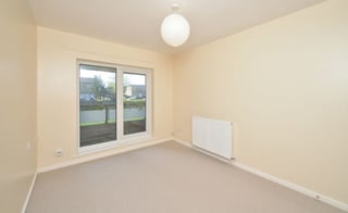Empty beige room with large glass doors, white ceiling light, radiator, and beige carpeted floor