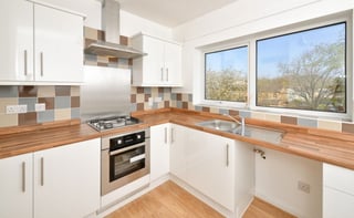 Modern white kitchen with wooden countertops, built-in stove, and large windows overlooking trees