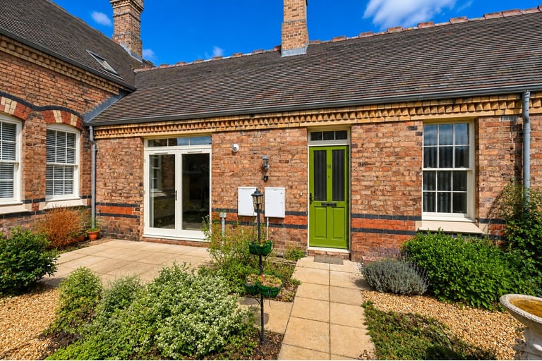 Brick cottage exterior with lime green door, white windows, paved patio, landscaped garden, and clear blue sky