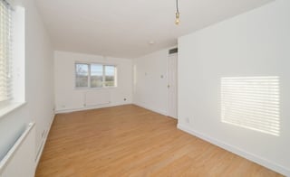 Empty room with wooden floor, white walls, windows, and a white door