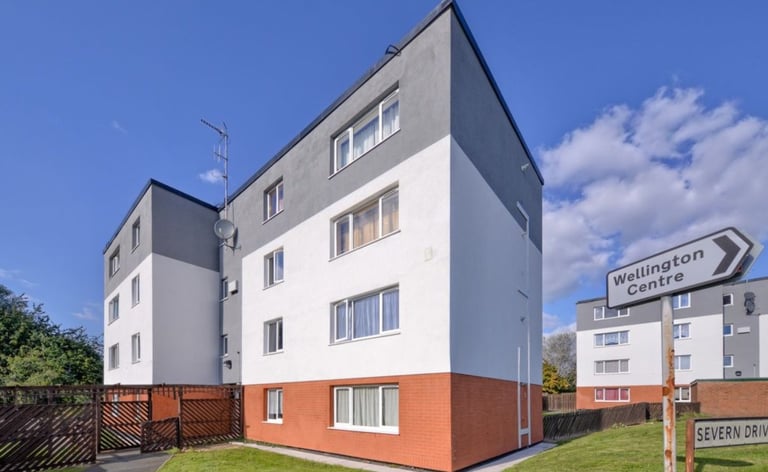 Modern apartment building with orange base and white upper levels against blue sky with green lawn in foreground